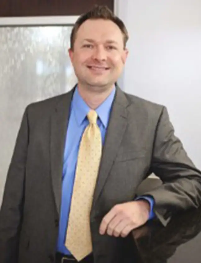Professional man in business attire smiling at camera in office setting.